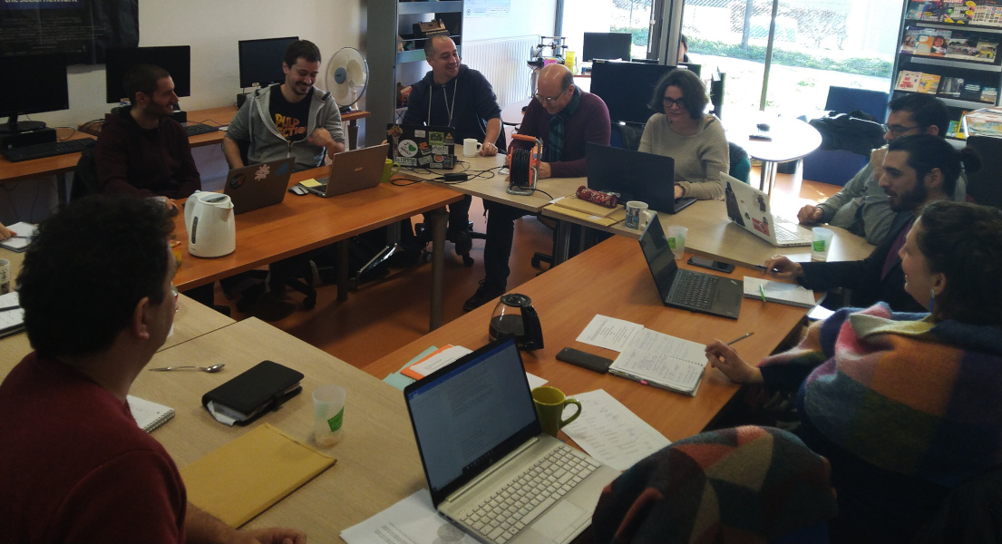 Photo d'une rencontre de médiateurs, des tables sont disposées en rectangle, une douzaine de personnes sont assises devant leur portable, cela semble joyeux.