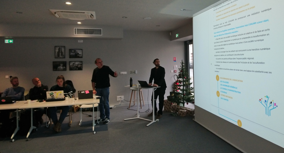 Photo issue de l'AG constitutive, on y voit un diaporama projeté avec le logo du hub, deux personnes debout et plusieurs personnes assises qui écoutent ou prennent des notes. 